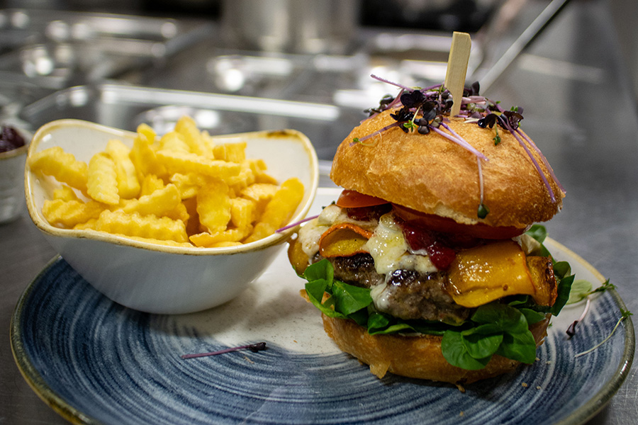 Hausgemachter Burger mit Käse, Salat und gegrilltem Kürbis, dazu Pommes, im Gasthof Reblitz in Nedensdorf.