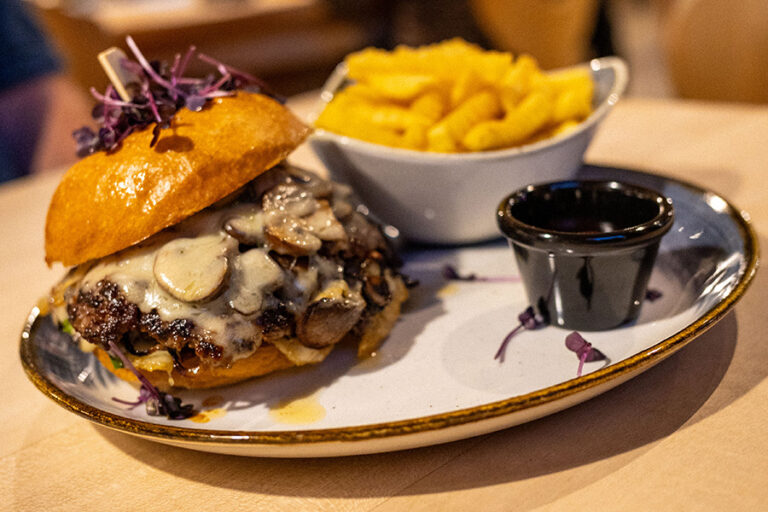 Saftiger Burger mit geschmolzenem Käse und Pilzen, serviert mit Pommes und Dip im Gasthof Reblitz in Nedensdorf.